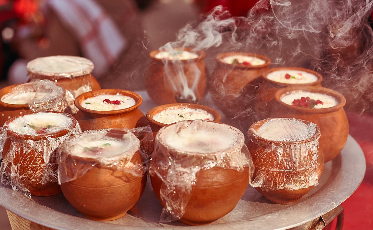 services-03 Close-up of steaming Indian desserts in clay pots, infused with aromatic spices and garnished with nuts.