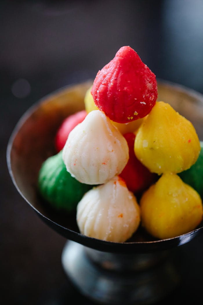 Vibrant close-up of stacked modak sweets in a metal bowl, symbolizing festive Indian cuisine.